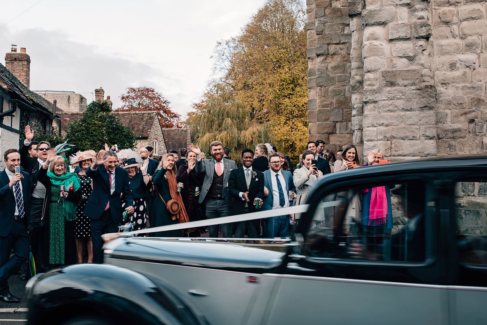 Documentary style wedding photograph of the wedding car driving off as the guests wave at it