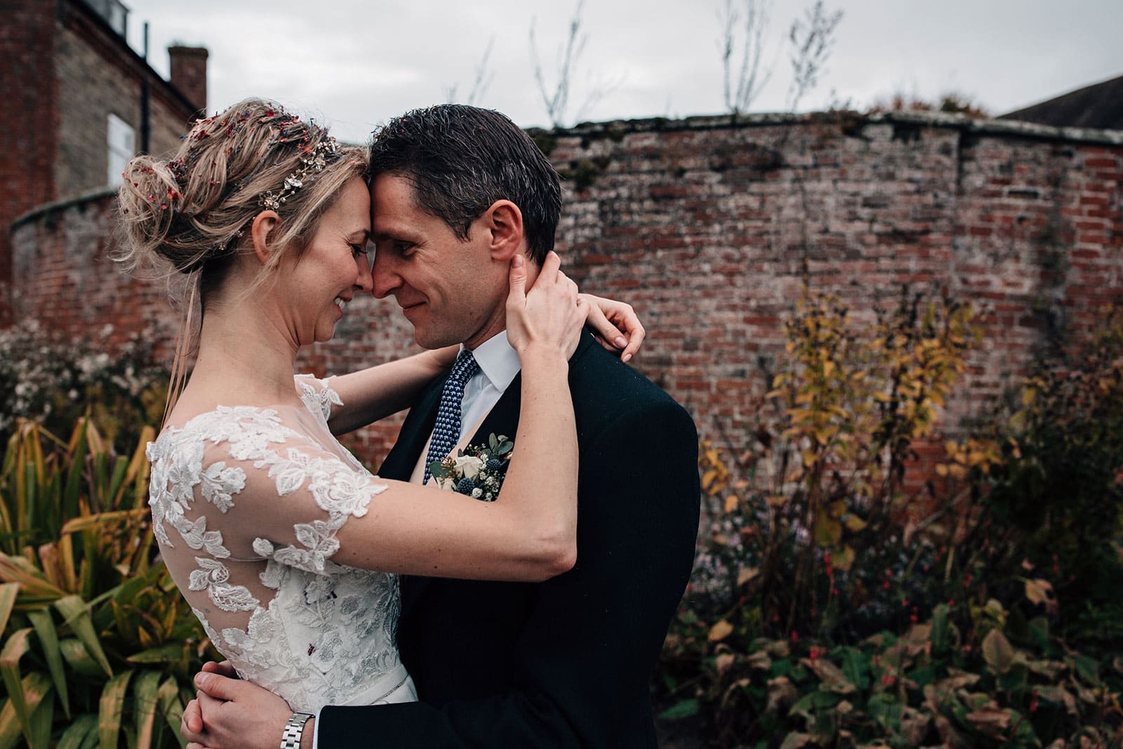 Couple embrace in front of a red brick wall at Delbury Hall in Shropshire