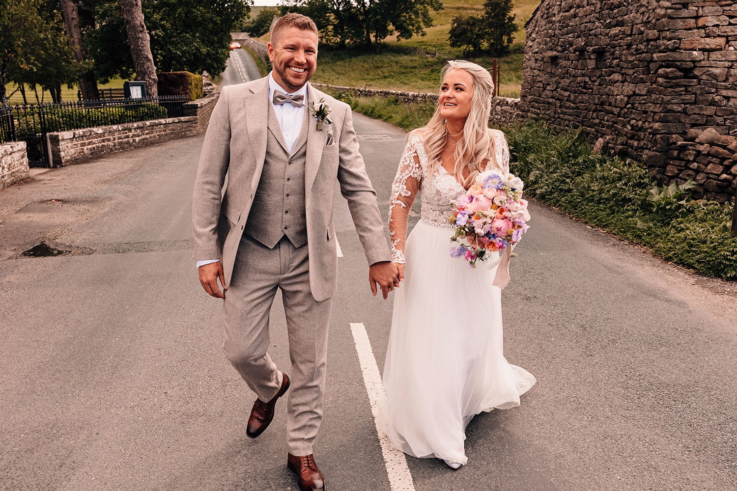 Relaxed photograph of a Bride and Groom walking down the road outside Yorebridge House in the Yorkshire Dales