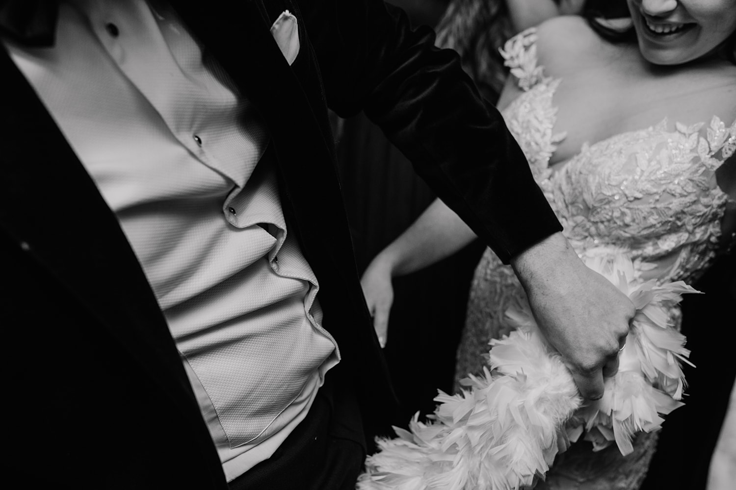 Black and white, close up image of the bride and groom dancing wildly with a feather boa