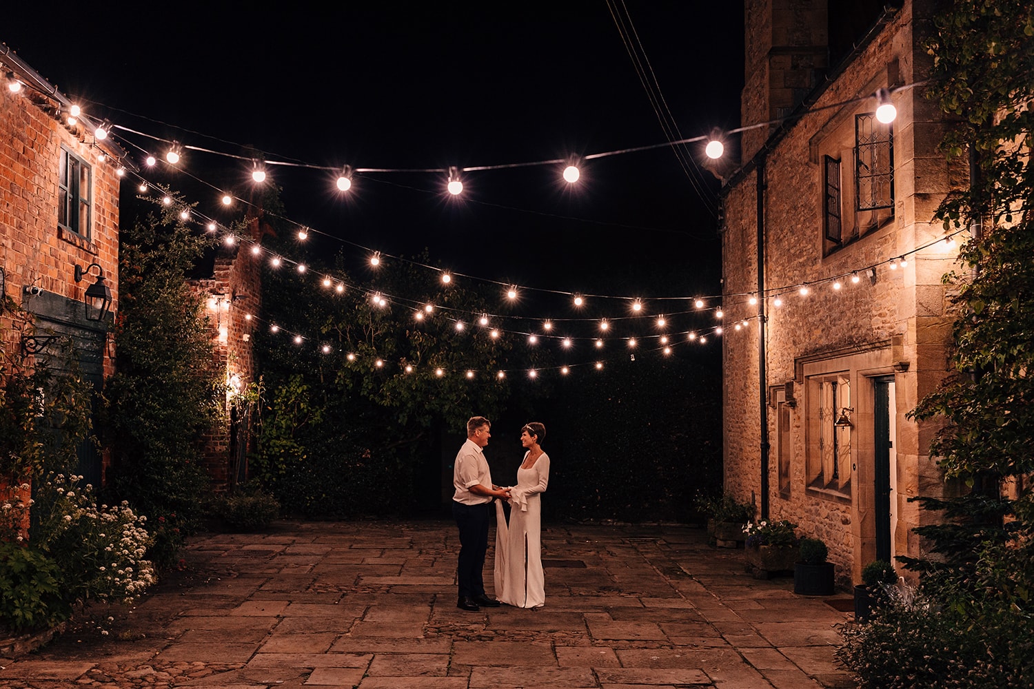 Evening photograph of the Bride and Groom under strings of festoon lights