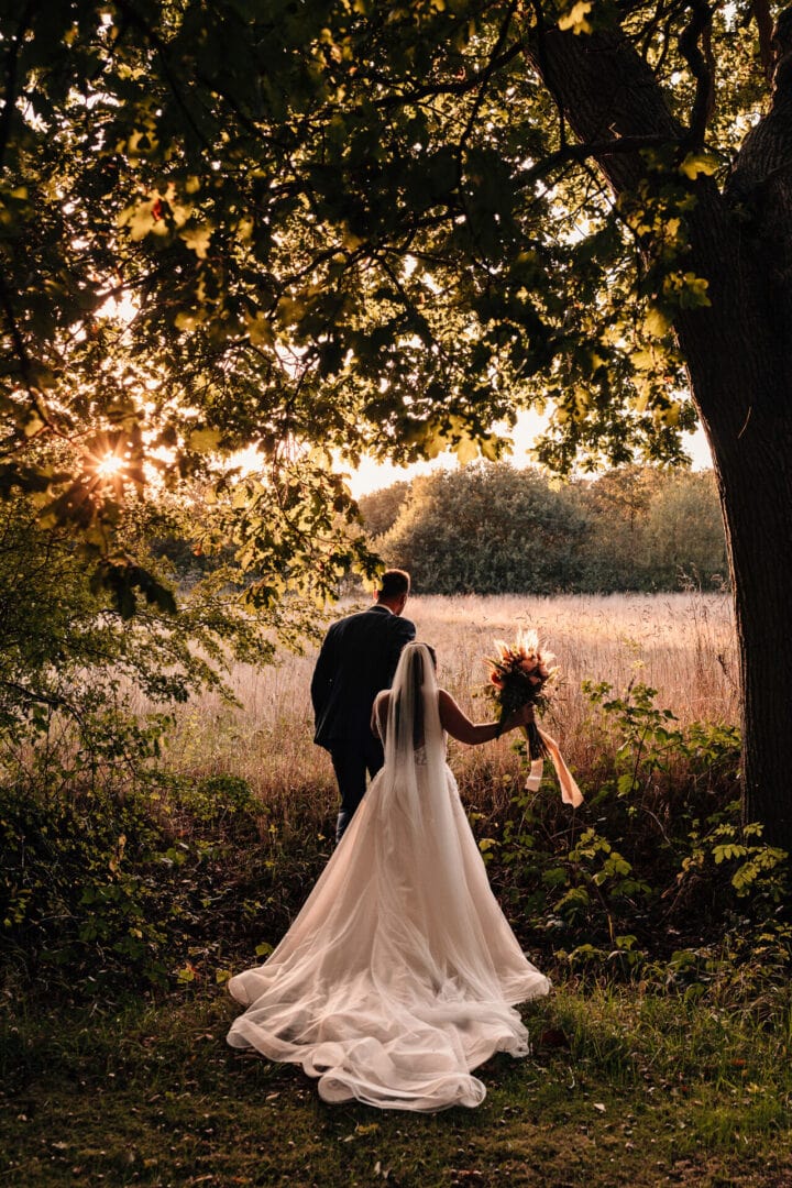 Documentary wedding photograph of a Bride and Groom walking away from the camera into a field