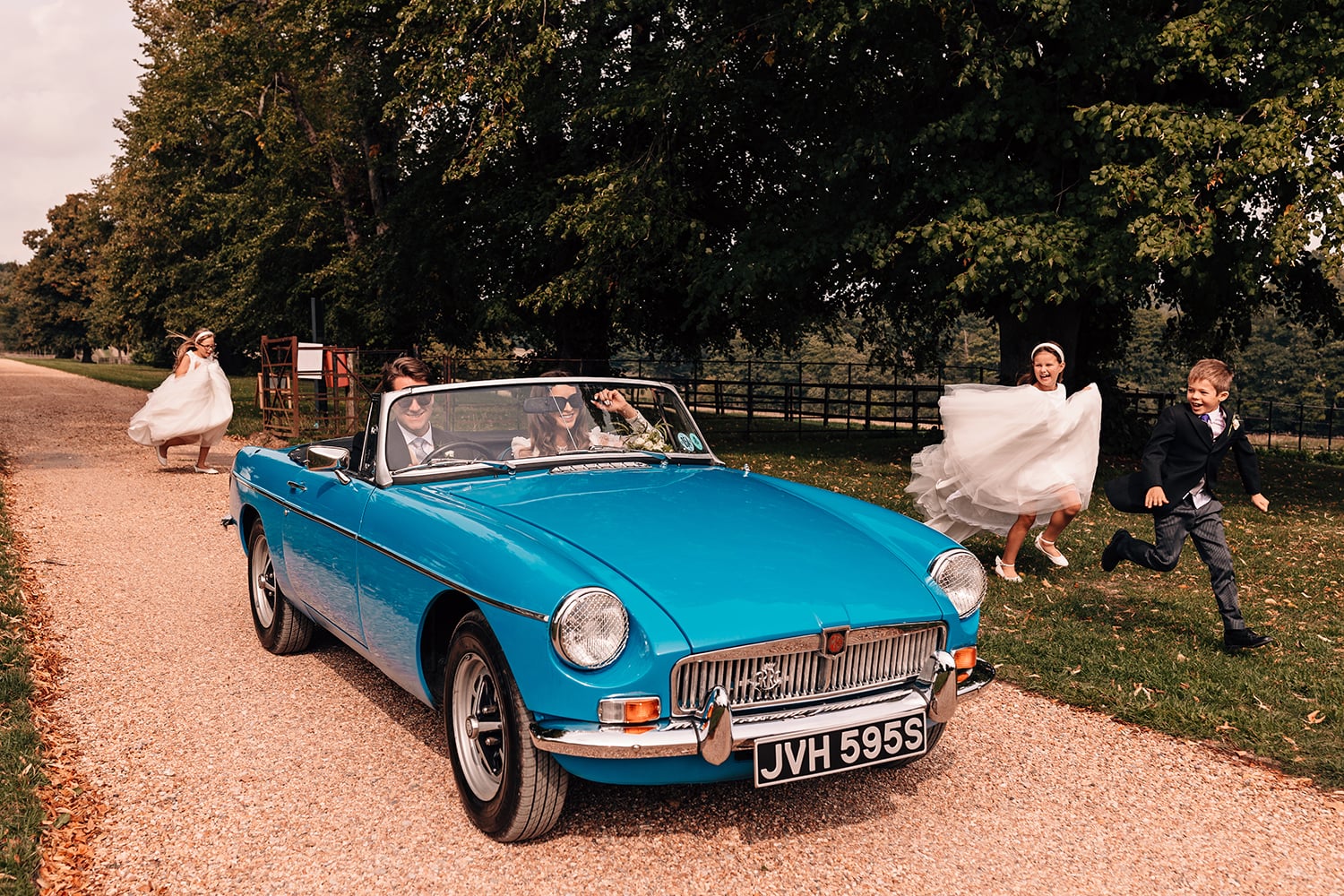 Children running alongside a vintage car with the Bride and Groom in