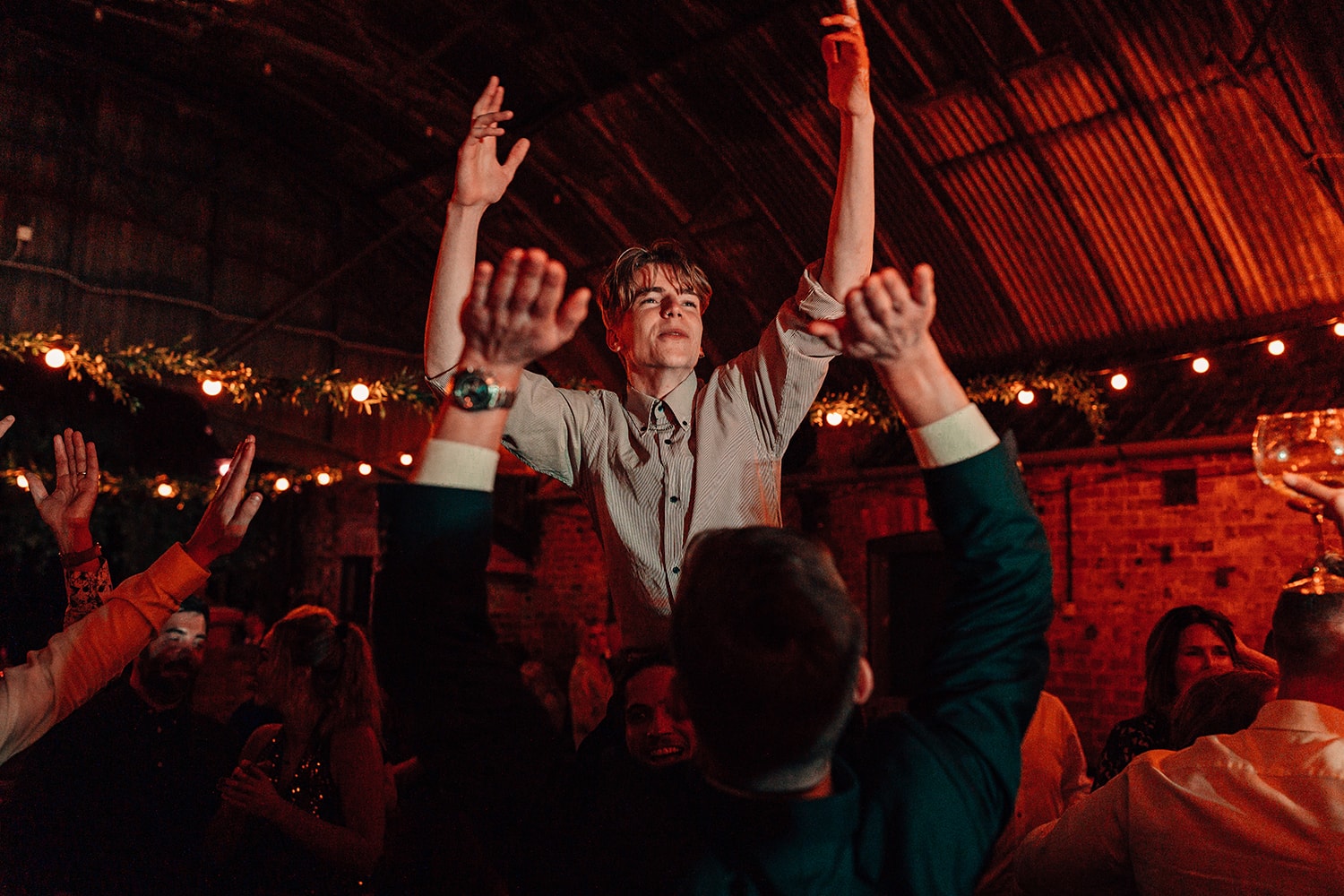 Male wedding guest partying hard and being lifted up on friends shoulders