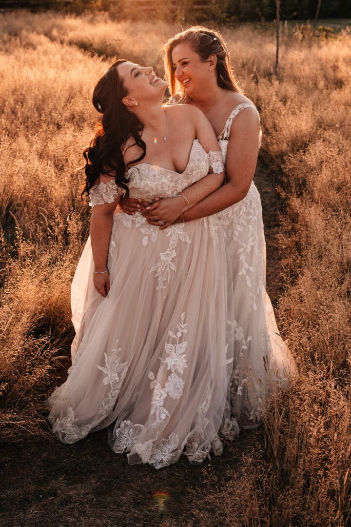 Two brides cuddling and laughing in a golden field at sunset
