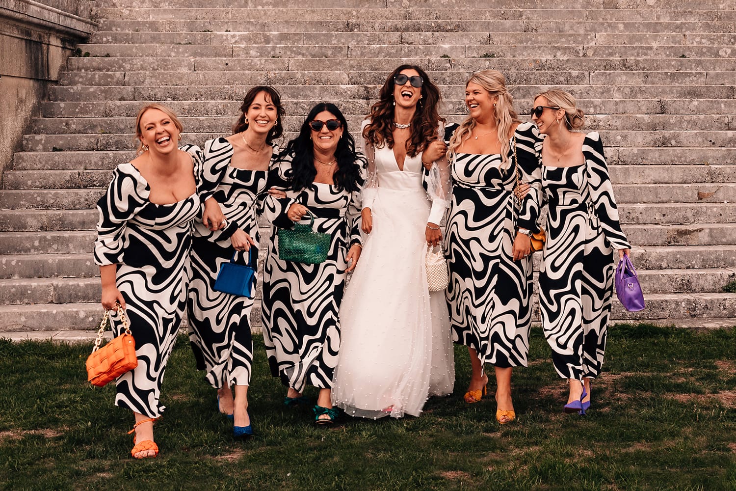 Natural photograph of a Bride and her bridesmaids in designer dresses laughing with one another