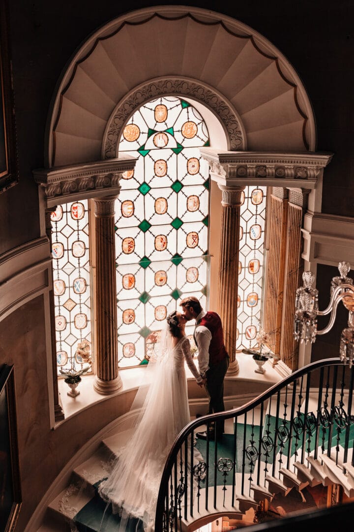 Romantic photograph of bride and groom in front of a grand castle stained glass window