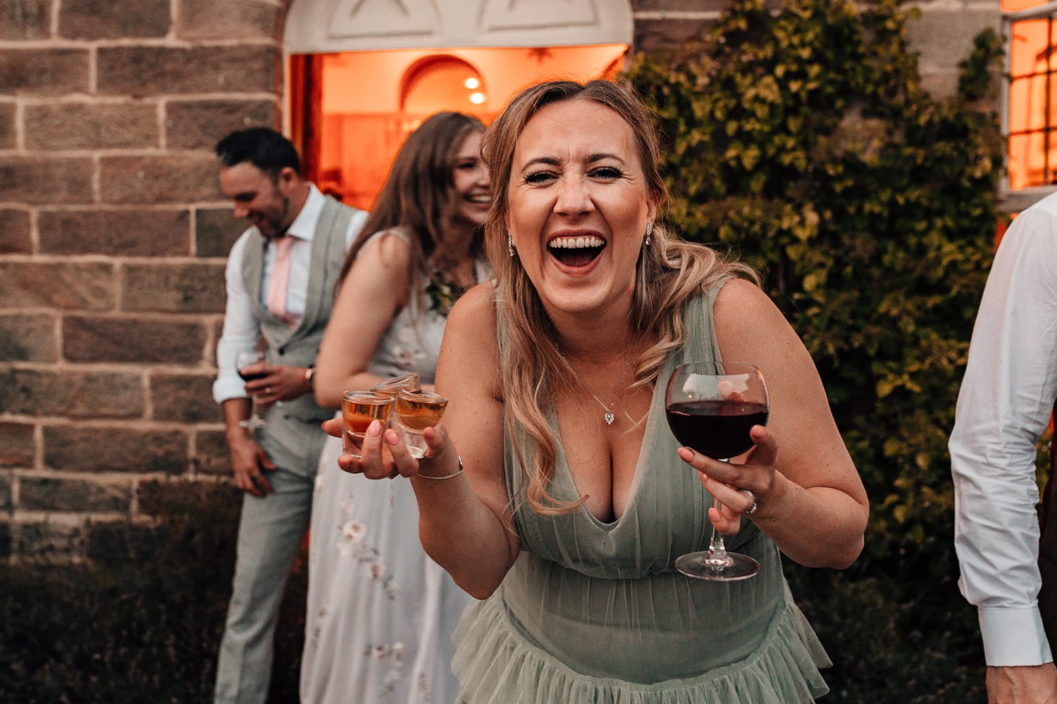 Candid wedding photograph of a wedding guest with three tequilas in her hands