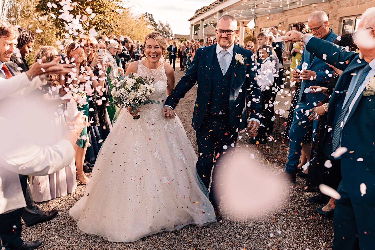 Bride and Groom walking under a shower of confetti thrown by their guests