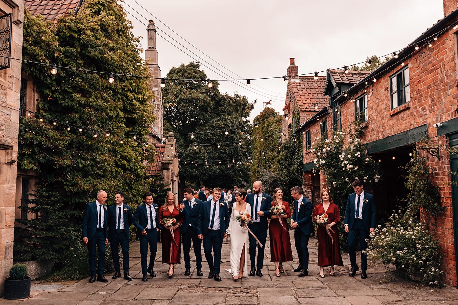 Relaxed group photograph of the Bridesmaids and Ushers walking toward the camera, chatting and laughing